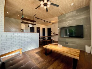 A modern interior with a wooden ceiling, a brick wall, a wooden bench, a table, and a mounted TV. - Ishigaki Villa Musubu (Ishigaki)