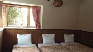 A room with two beds, wooden headboard, a window with curtains, and a wall-mounted lamp. - Pension Mogu (Shinano)