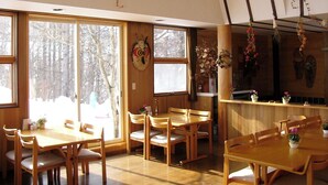 A dining area with wooden furniture, large windows, and a view of trees. - Pension Mogu (Shinano)