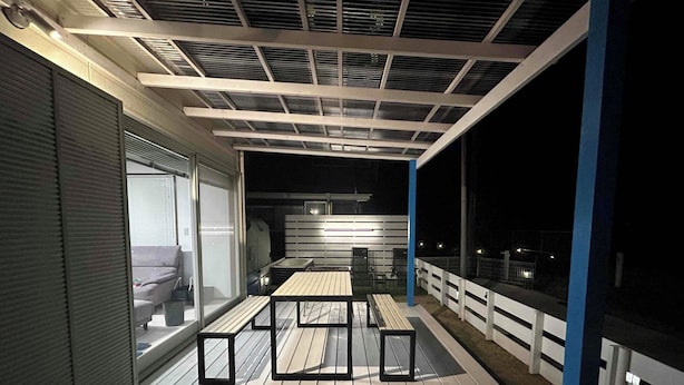 Una terraza exterior con una mesa y sillas, un área cubierta con techo, y vista al mar.