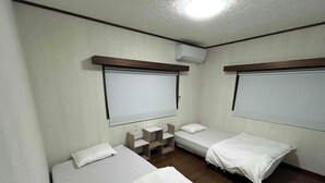 Una habitación pequeña y limpia con dos camas individuales, una mesita y una ventana.