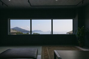 Ein Zimmer mit großem Fenster mit Blick auf eine gebirgige Landschaft und ein Gewässer.