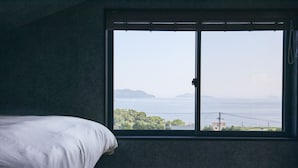 Un dormitorio con un ventanal grande, una cama y vistas al mar y la costa distante.