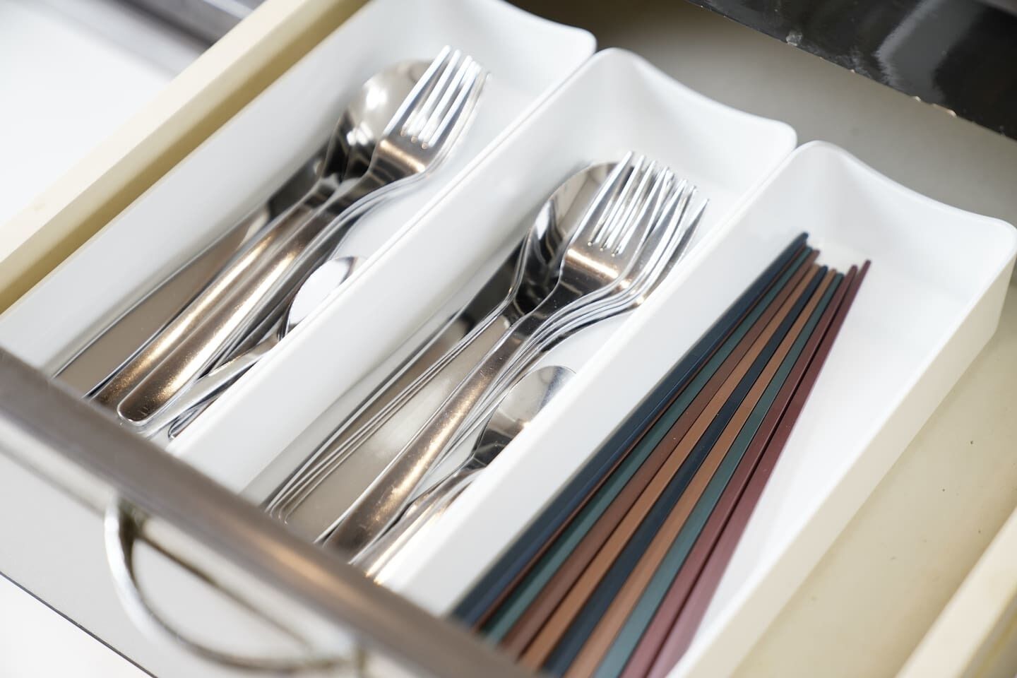 A drawer containing neatly arranged silverware and a set of colored napkins.