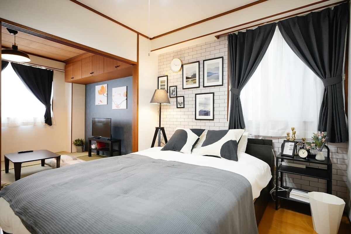 A modern hotel room with a large bed, a TV, a desk with a lamp, and artwork on the walls.