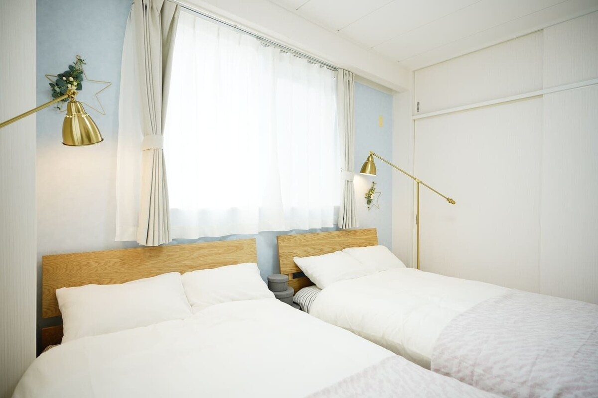 A bedroom with two beds, a window with curtains, a bedside lamp, and a star decoration on the wall.