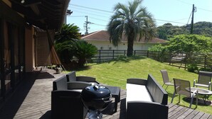 Una terraza con mobiliario exterior, una parrilla y vistas a una casa y palmeras.