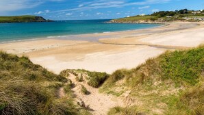 Une plage côtière avec un ciel dégagé, des rivages sablonneux et des dunes herbeuses.