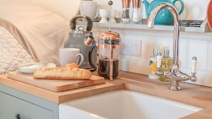 Une cuisine équipée d’une machine à café, d’une théière, d’une bouteille d’huile et d’une miche de pain posée sur le comptoir.