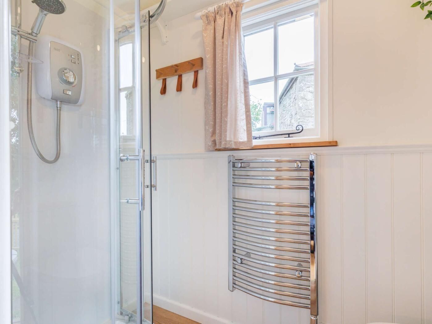 Een badkamer met een douchecabine van glas, een handdoekrek, een raam met gordijn en een handdoekwarmer.
