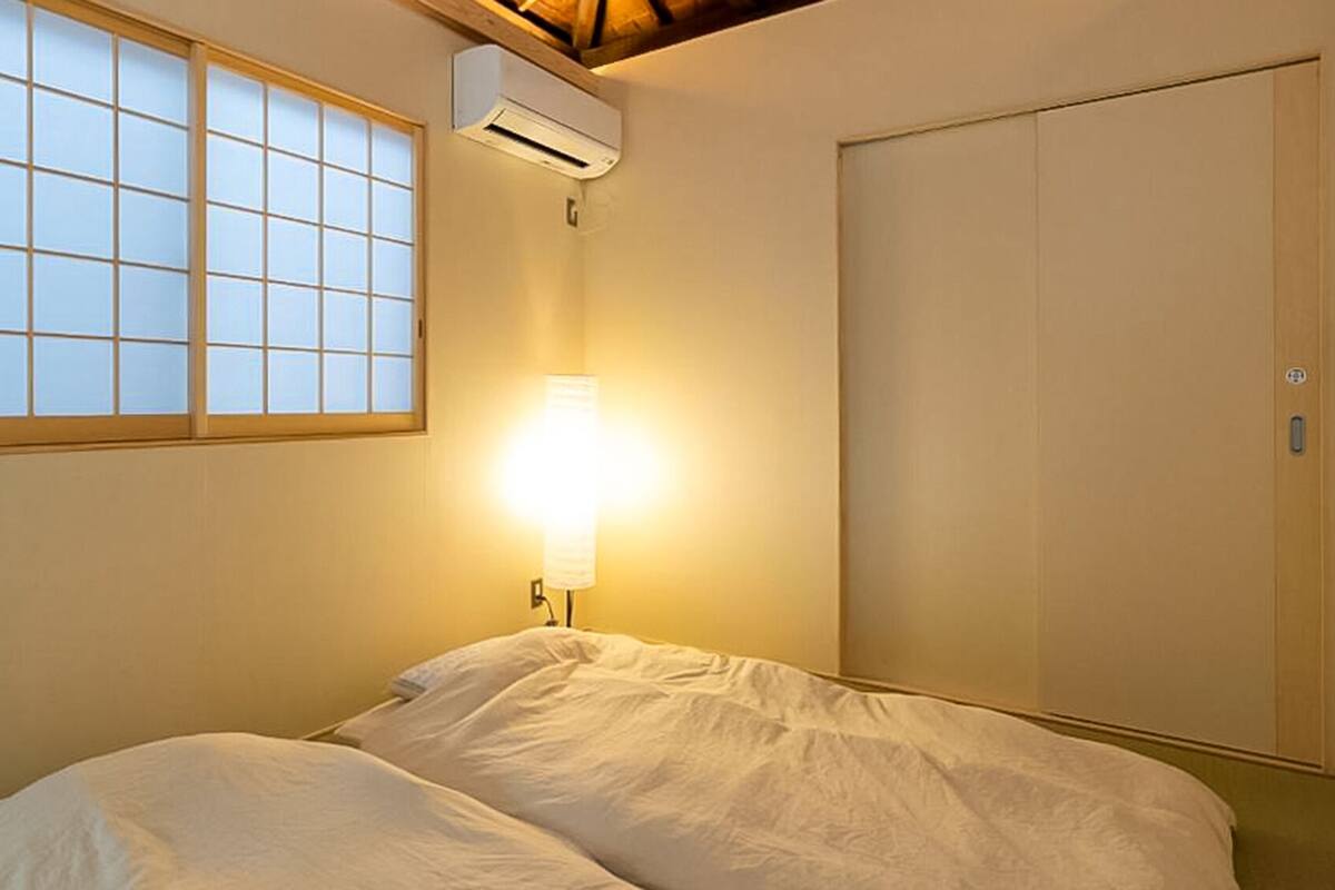 A room with a bed, a window with a grid pattern, an air conditioning unit, and a wardrobe.