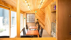 A wooden interior with a dining table and chairs, a bookshelf, and a door with a window. - Trawl (Kamakura)