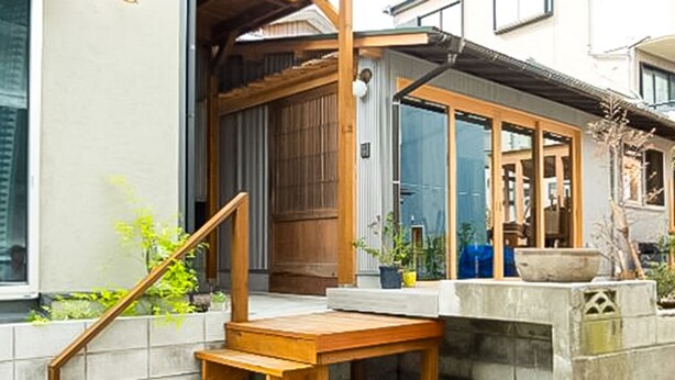 A traditional Japanese house with a wooden entrance, sliding doors, and a small garden area with plants and a wooden bench. - Trawl (Kamakura)
