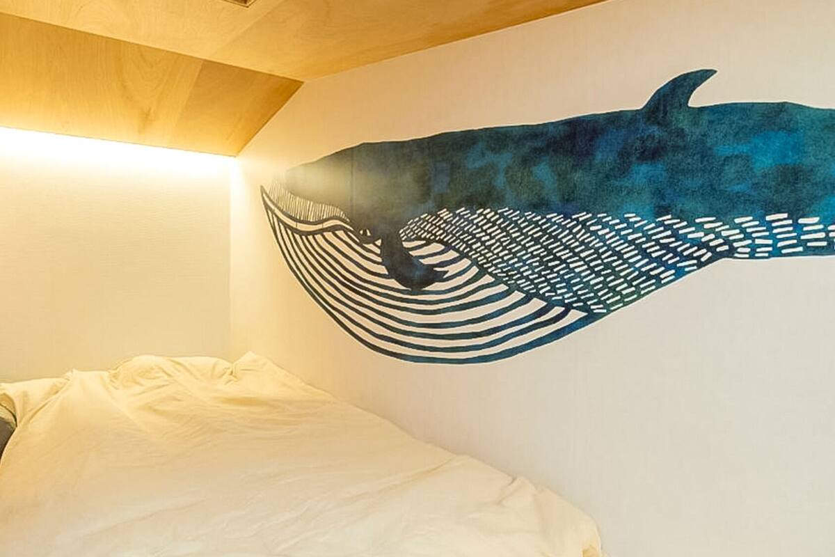 A room with a bed, a wall mural, and a wooden ceiling.