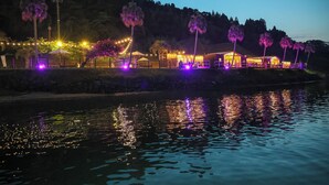 Hotel a orillas del río con varias edificaciones conectadas, un muelle y palmeras.