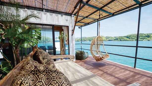 Habitación con un gran ventanal que da a un cuerpo de agua, un sillón colgante y un sofá estampado.
