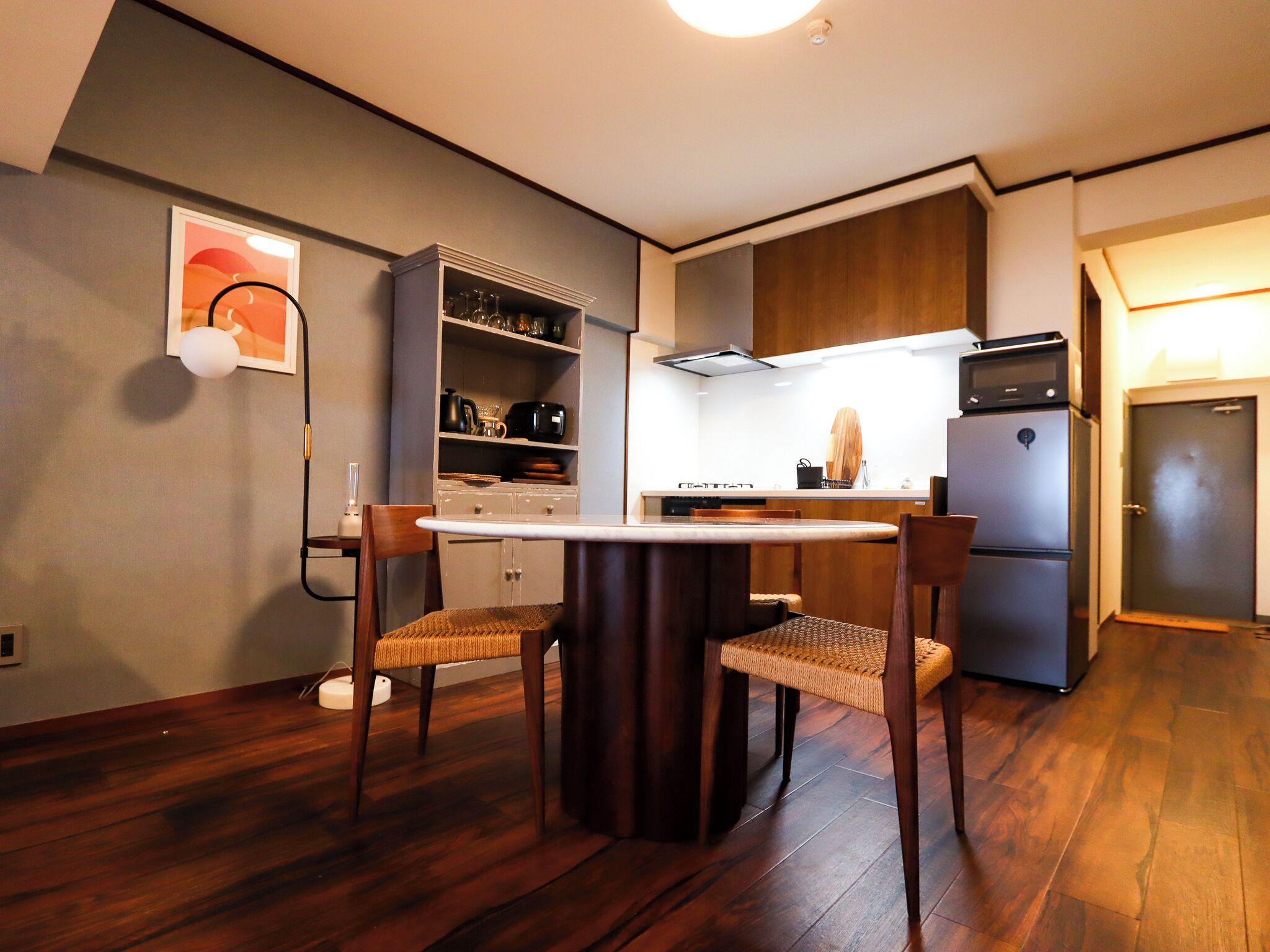 A compact kitchen with wooden cabinets, a built-in microwave, and a dining area with a round table and two chairs.