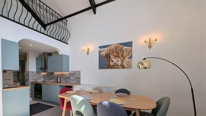 A dining area with a wooden table, four chairs, a kitchen in the background, and a staircase. - 3 Bed in Windermere (oc-sz469) (Windermere)