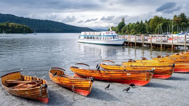 A lake with boats docked at a pier, a large white boat in the water, and a forested hill in the background. - 3 Bed in Windermere (oc-sz469) (Windermere)