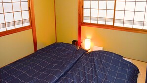 Habitación pequeña con una cama individual, estructura de madera, mesita de noche, lámpara y ventana con diseño de celosía.