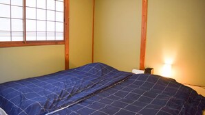 Habitación pequeña con cama individual, vigas de madera, ventana con diseño de celosía y lámpara de noche.