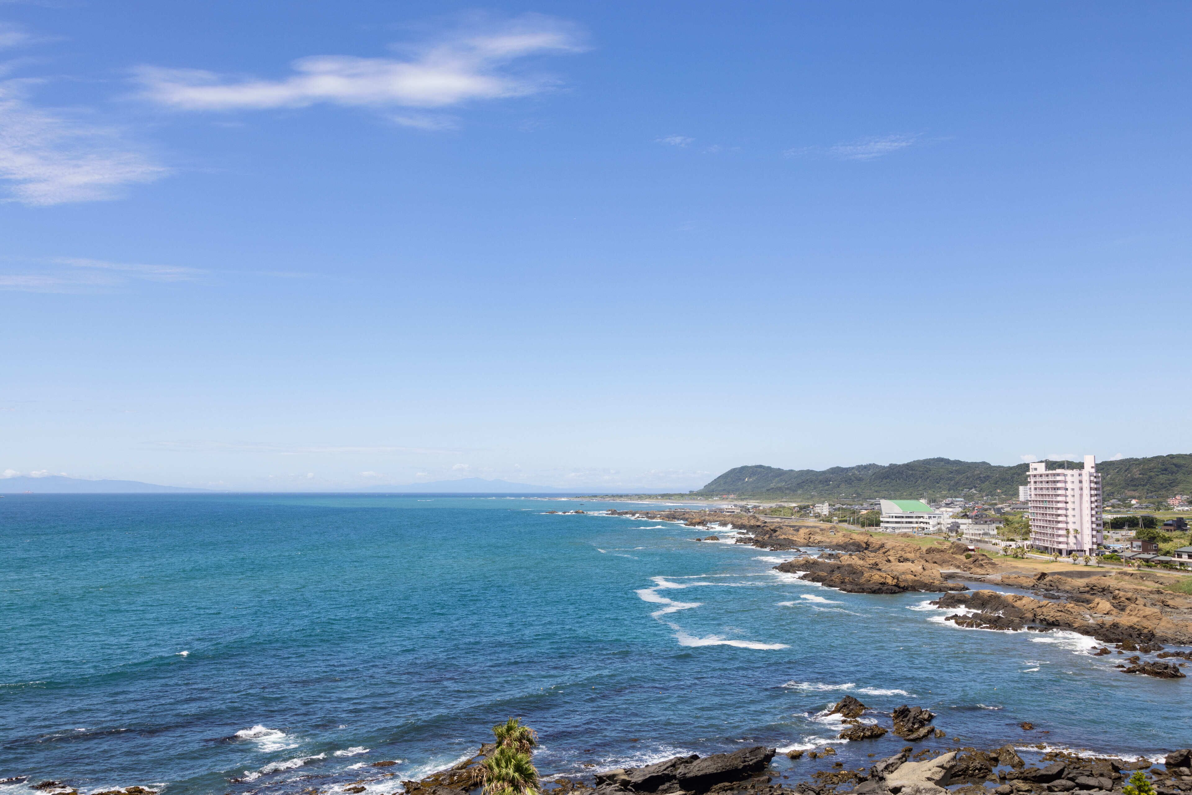 A coastal view with a hotel, rocky shoreline, and ocean waves.
