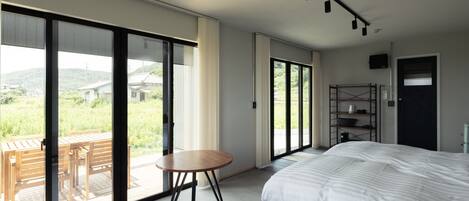 Une chambre dotée d’un grand lit, d’une petite table et offrant une vue sur l’extérieur grâce à de grandes portes coulissantes.