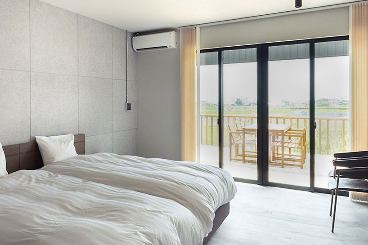 A hotel room with a large bed, a flat-screen TV, a sliding glass door to a balcony with outdoor furniture.
