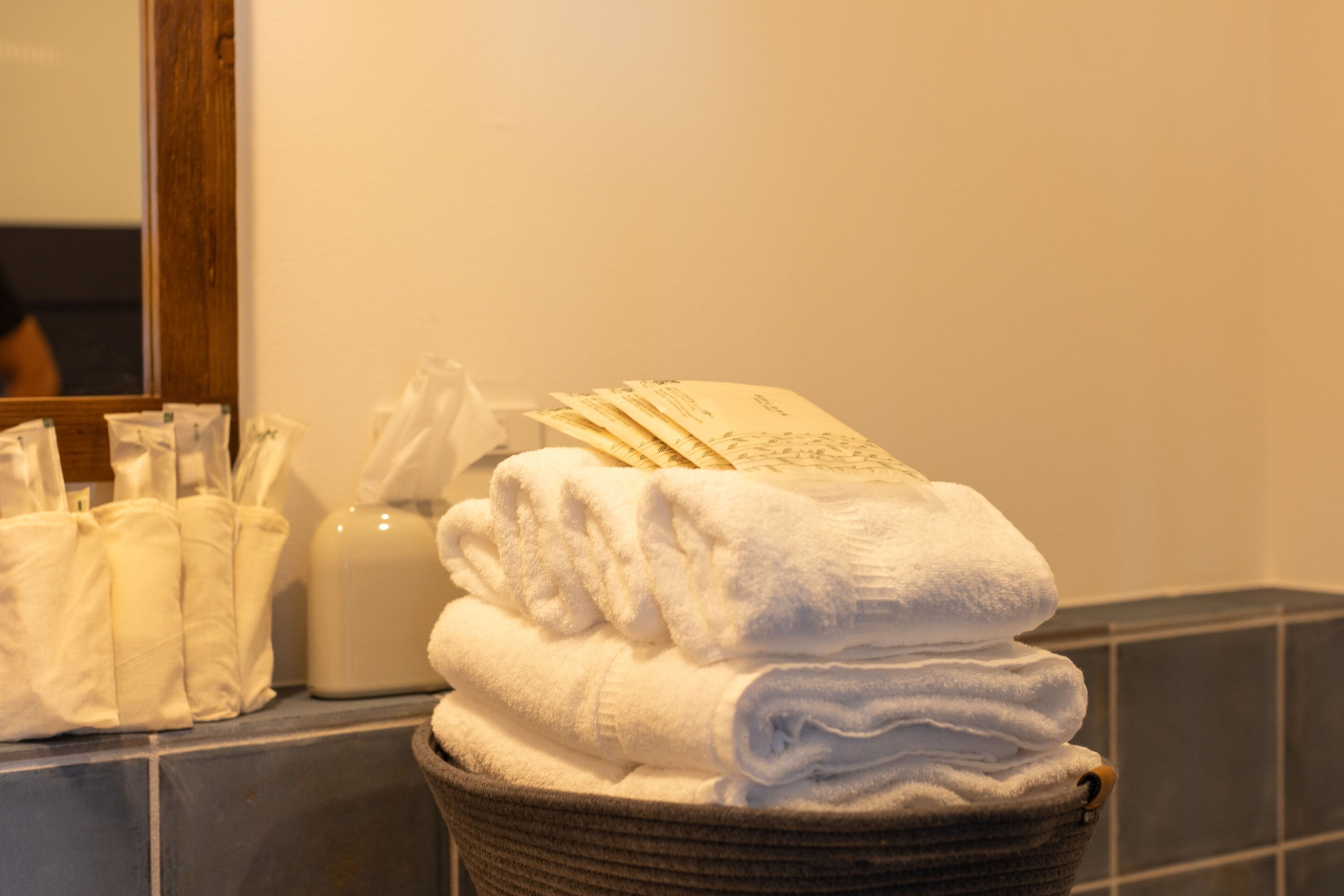 A stack of white towels in a basket, a bottle of lotion, and a tissue box on a bathroom counter.