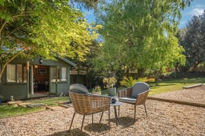 A cozy outdoor seating area with wicker chairs and a table, a small shed with a door, and a well-maintained garden. - 1 Bed in Sandown (oc-85248) (Sandown)