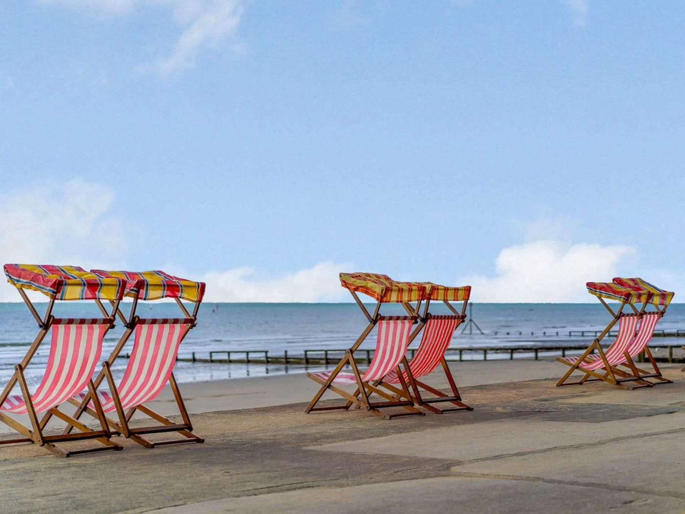 Beach chairs with striped cushions aligned along a promenade by the sea.