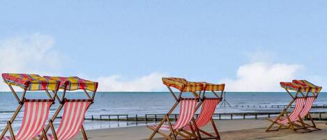Beach chairs with striped cushions aligned along a promenade by the sea.