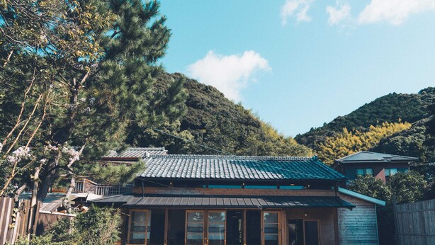 A traditional Japanese house with a tiled roof, wooden structure, and a view of a forested hillside. - Tsumugiyado Fuji (Fujieda)