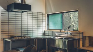A kitchen with a gas stove, stainless steel sink, and a window with a view of greenery. - Tsumugiyado Fuji (Fujieda)