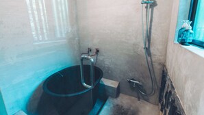 A bathroom with a bathtub, a shower, and a window with toiletries. - Tsumugiyado Fuji (Fujieda)