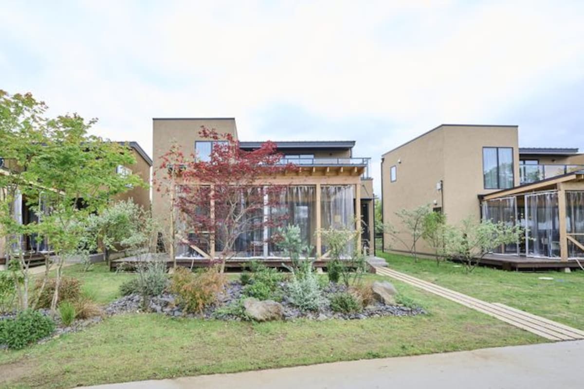 A modern building with large windows, a well-maintained garden, and a clear sky.