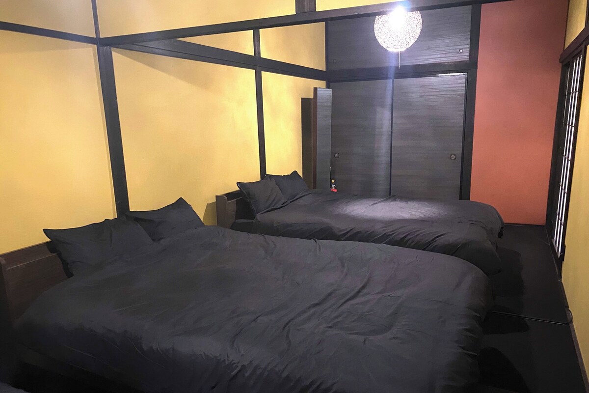 A room with two beds, a dark wooden headboard, a wall-mounted light fixture, and a door with a circular glass panel.