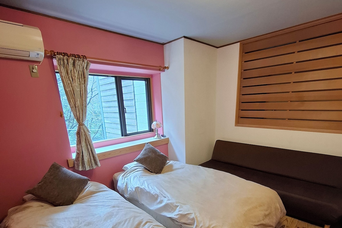 A bedroom with two beds, a window with curtains, a ceiling fan, and a wooden floor.
