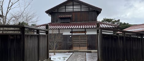 Un bâtiment traditionnel en bois, avec un toit recouvert de tuiles, une porte en bois et un sol enneigé.
