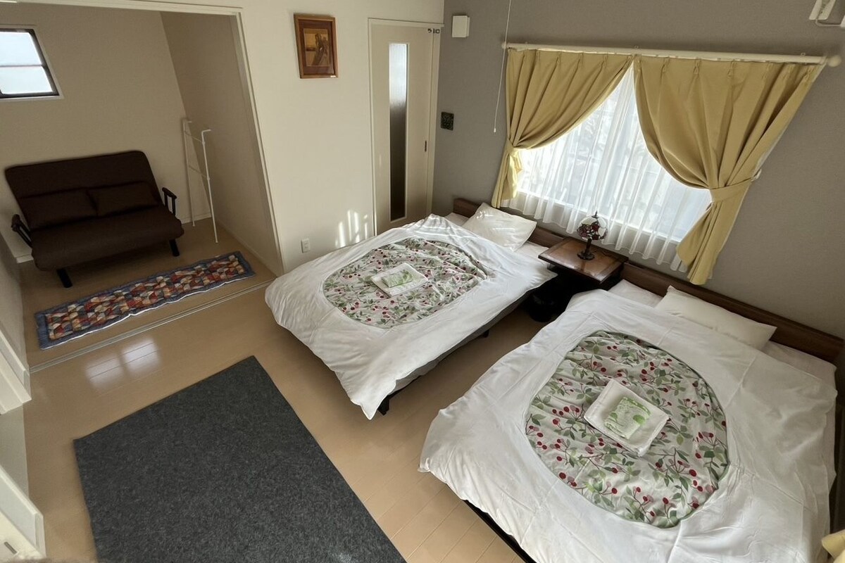 A room with two beds, a sofa, a window with curtains, a door, and a small rug.