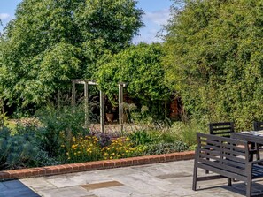 Een tuin met een pergola, een bakstenen rand en een tafel met stoelen.