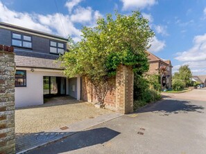 Een woonstraat met huizen, een verharde oprit en een boom voor een van de huizen.