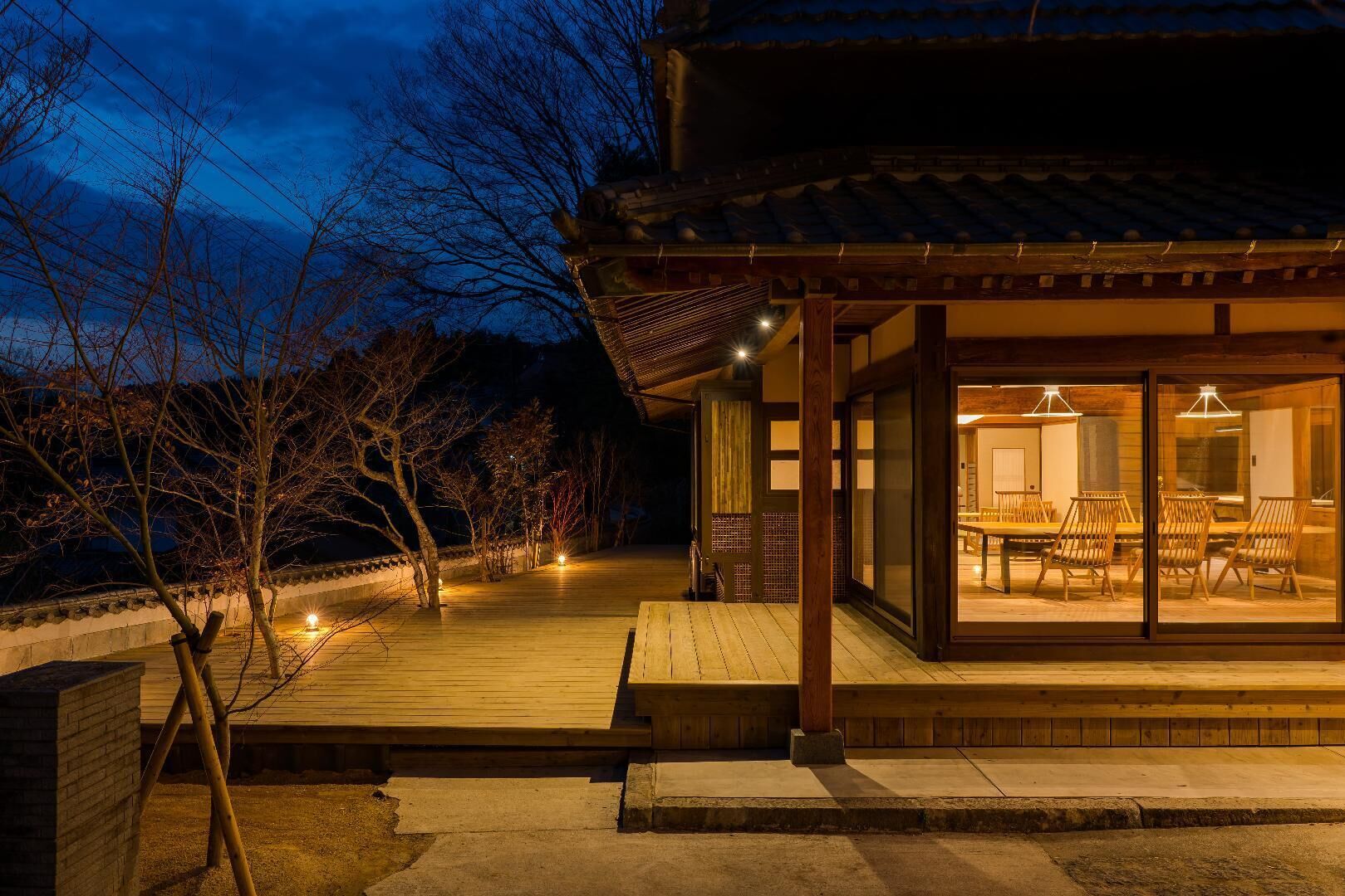 A traditional Japanese-style building with a wooden deck, a dining area with tables and chairs, and a view of the surrounding trees.