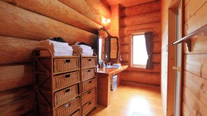 A wooden cabin interior with a wooden floor, a sink, a mirror, and wicker baskets filled with towels.