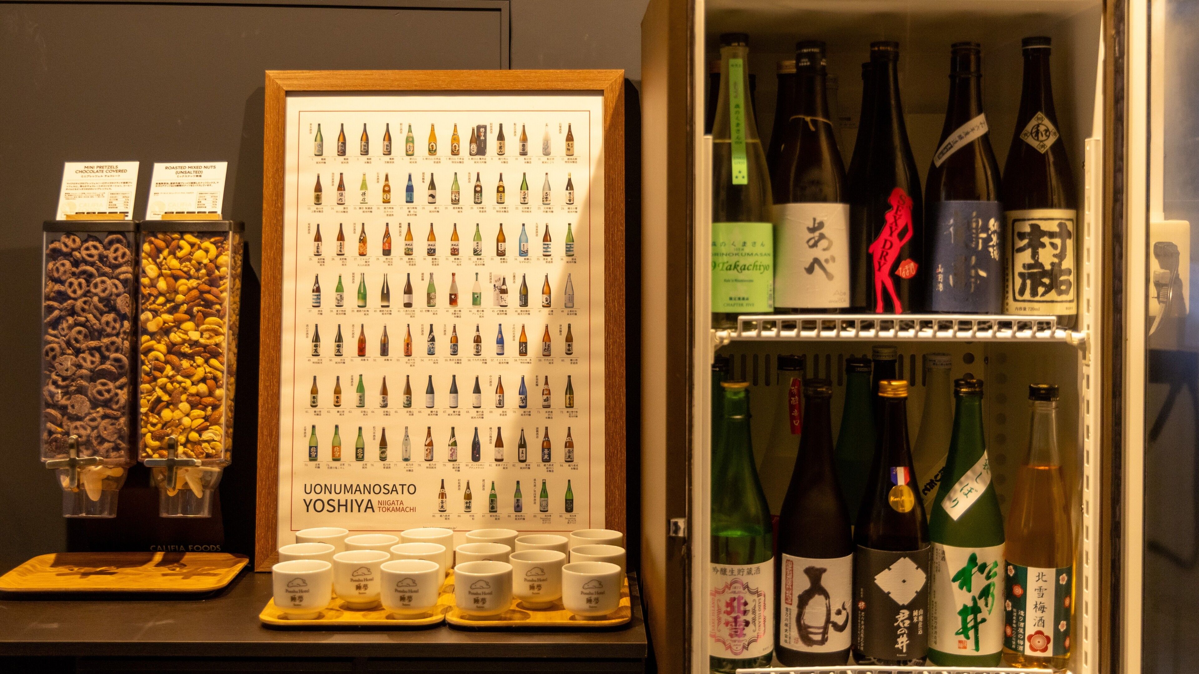 A display of various Japanese snacks and beverages, including a framed menu and a selection of sake bottles.