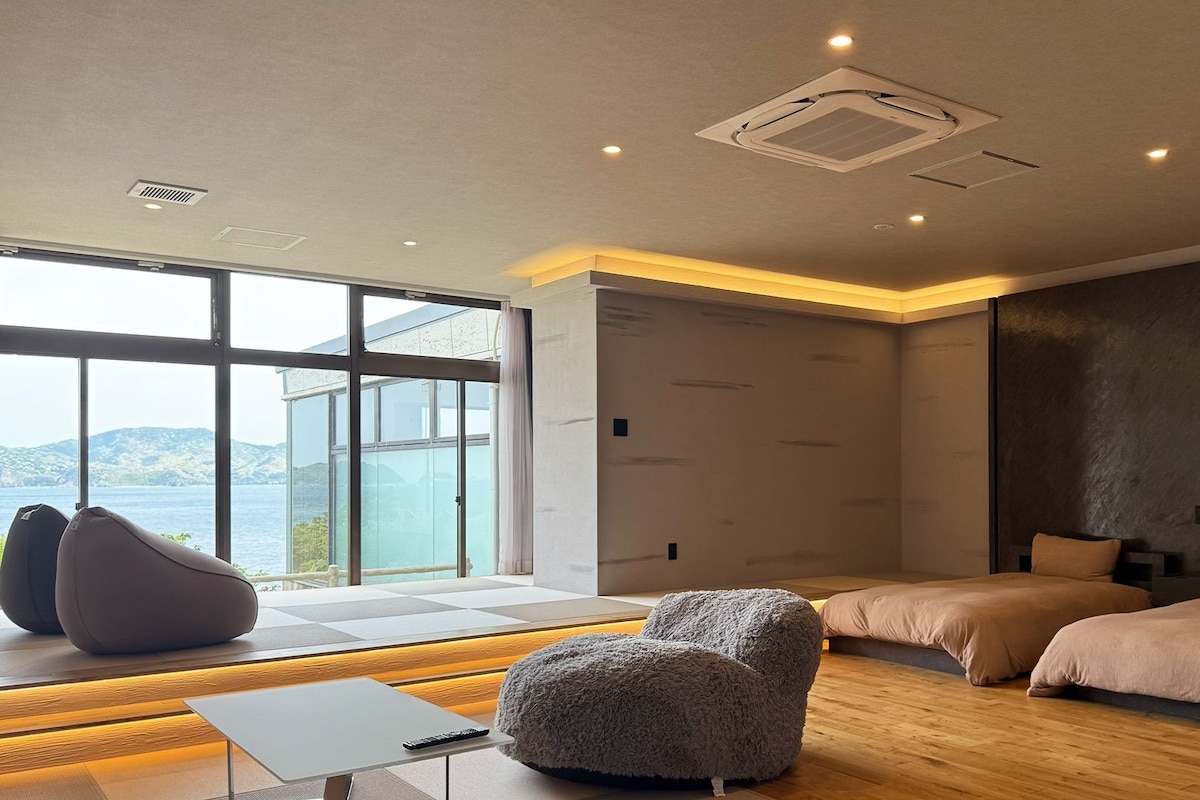 A modern bedroom with a large window, a bed, a chair, and a bedside table.