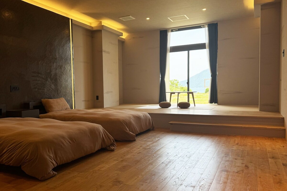Una habitación de hotel moderna con dos camas, un ventanal con vistas y una pequeña mesa junto a la ventana.