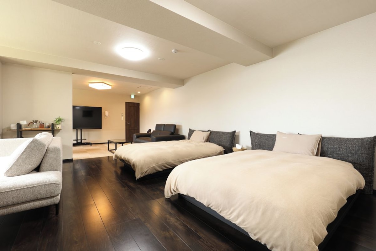 A hotel room with two beds, a sofa, a TV, and a desk.