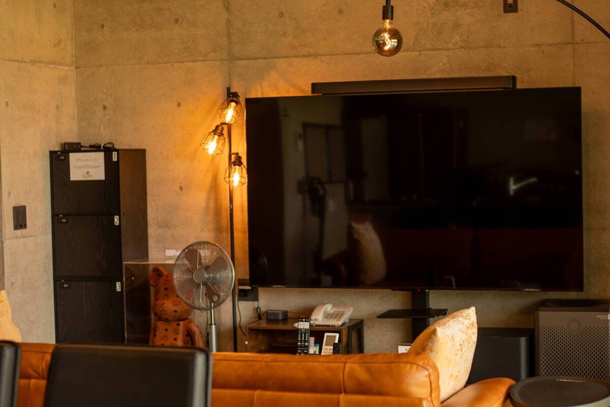 Un soggiorno con divano, una grande TV a schermo piatto, una ventola e un tavolino da caffè.