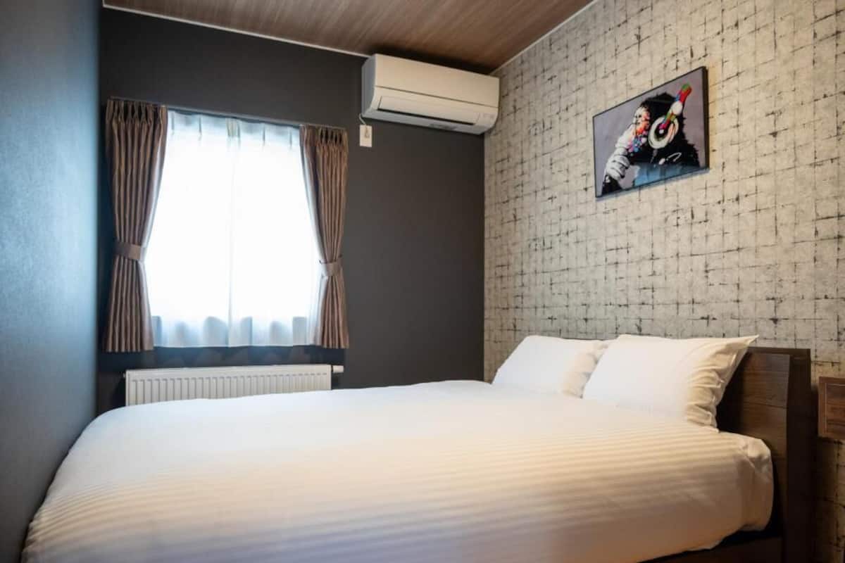 Ein Hotelzimmer mit Bett, einem fensterbelaubten Fenster, einer Klimaanlage und einer strukturierten Wand.